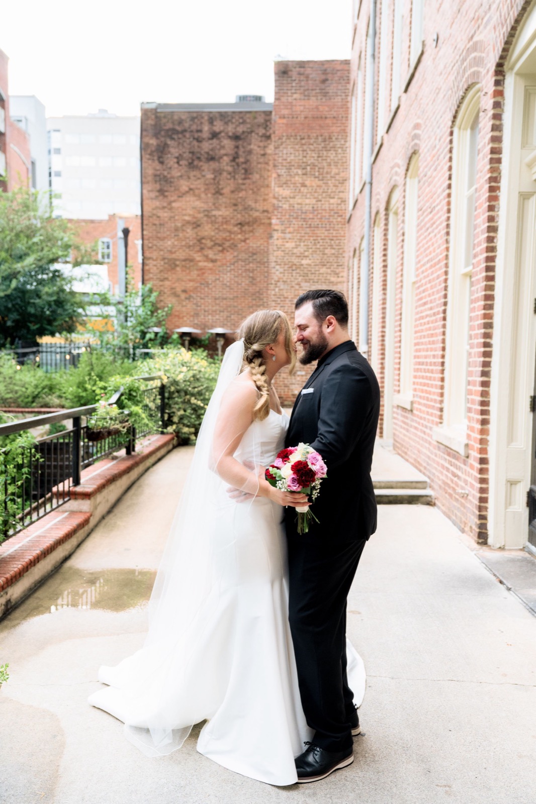 A newlywed couple sharing a kiss beside a brick building in downtown Raleigh